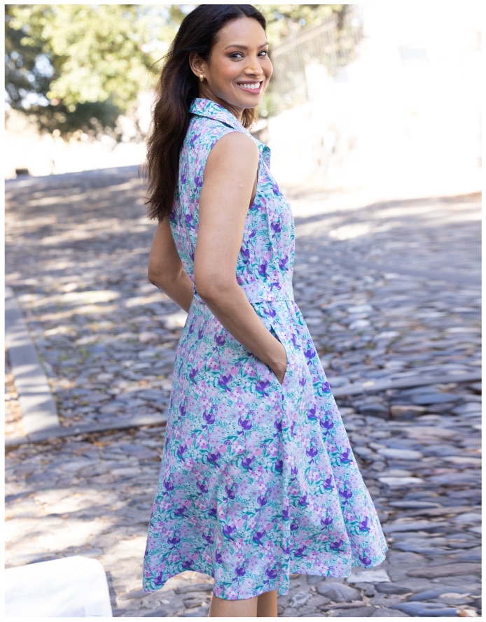 woman standing on paved road with hands in pockets wearing a floral dress in pueples and blues