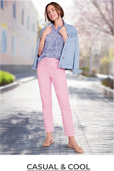 woman smiling, standing outside a house, wearing blue cardigan and pink pants