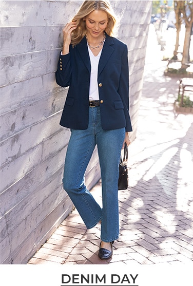 woman leaning a gainst a wall with a dark blue jacket, whie shirt and blue jeans.