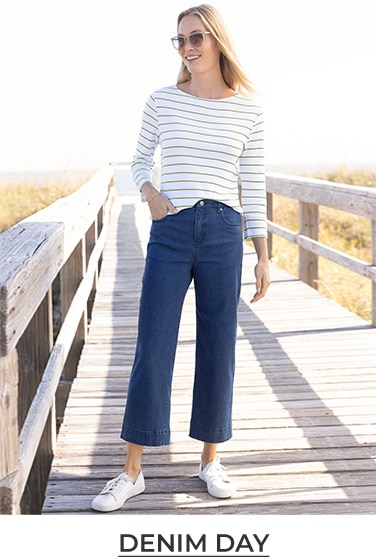 woman standing on a dock by the ocean wearing white and blue striped blouse and blue jeans