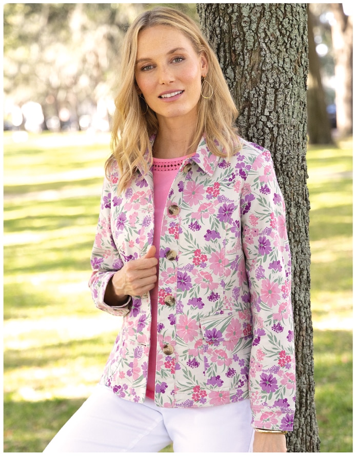 woman leaning on tree with floral print jackets and white pants