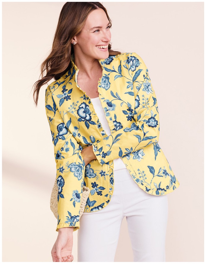 woman looking right and wearing a yellow jacket with blue floral prints nd white pants