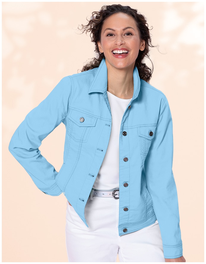 woman smiling into camera, wearing a light blue jean jacket and white pants